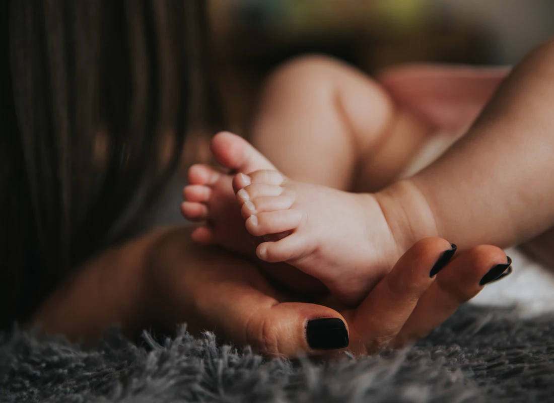 Mano adulta sosteniendo con cuidado los pies de un bebé